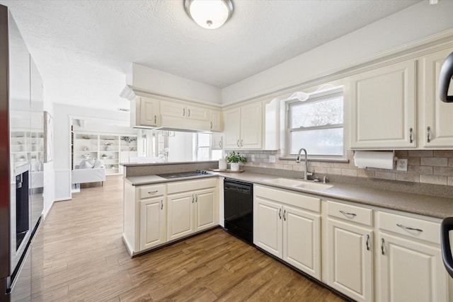 kitchen featuring a peninsula, wood finished floors, a sink, decorative backsplash, and black appliances