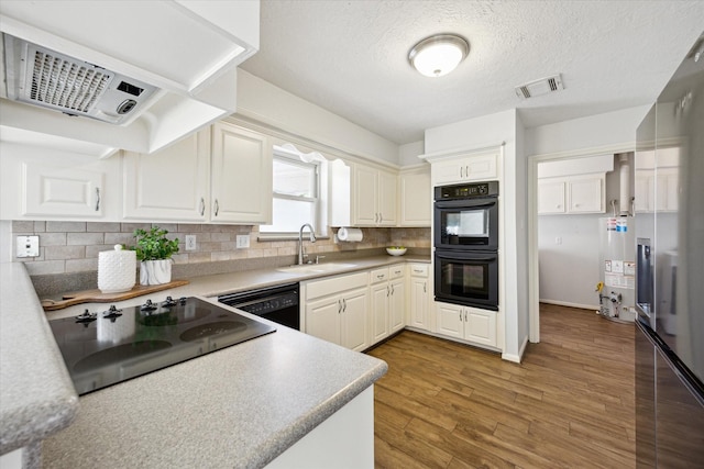 kitchen with a sink, range hood, light wood-type flooring, decorative backsplash, and black appliances