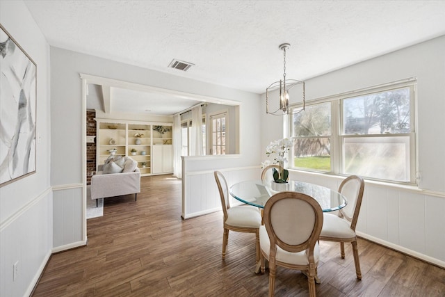 dining space featuring visible vents, a notable chandelier, a textured ceiling, and wood finished floors