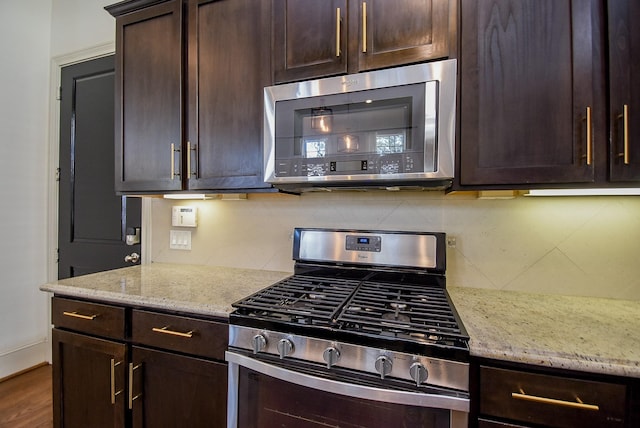 kitchen featuring stainless steel appliances, tasteful backsplash, dark brown cabinetry, and light stone counters