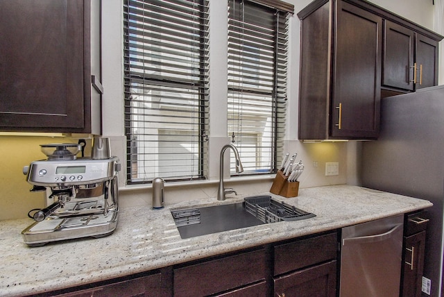 kitchen featuring light stone counters, appliances with stainless steel finishes, a sink, and dark brown cabinetry