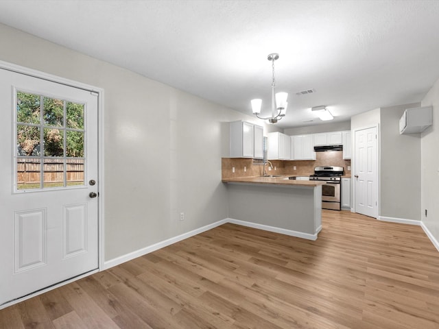 kitchen featuring a peninsula, a sink, visible vents, decorative backsplash, and gas stove