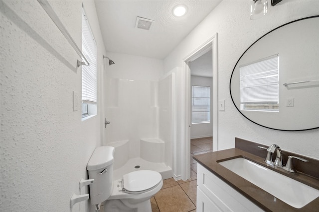 bathroom with a textured wall, toilet, vanity, tile patterned floors, and a stall shower