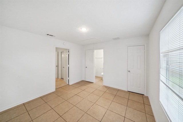 unfurnished bedroom with baseboards, light tile patterned flooring, visible vents, and attic access