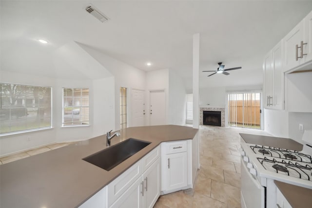 kitchen featuring white gas stove, a fireplace, a sink, visible vents, and a ceiling fan