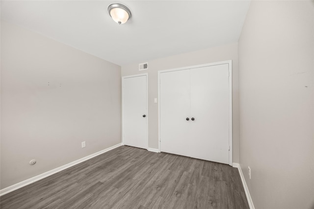 unfurnished bedroom featuring visible vents, baseboards, a closet, and wood finished floors