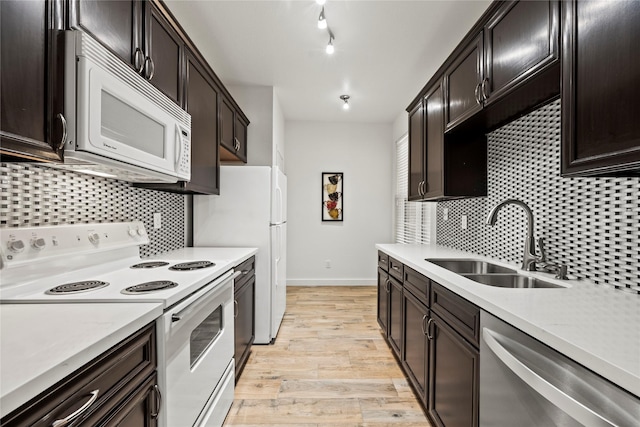 kitchen with light wood finished floors, light countertops, decorative backsplash, a sink, and white appliances