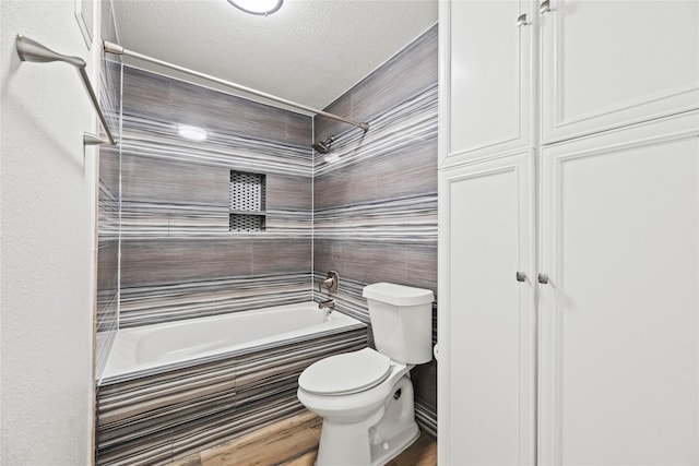 bathroom featuring toilet, tiled shower / bath, and a textured ceiling