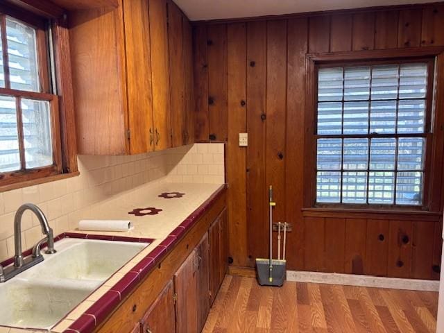 kitchen featuring wooden walls, a sink, light wood-style floors, decorative backsplash, and brown cabinetry