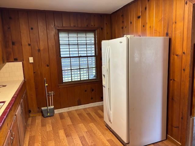 kitchen with white fridge with ice dispenser, wood walls, light wood-type flooring, and brown cabinetry