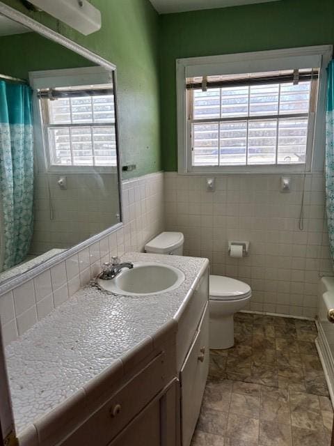 bathroom with toilet, a wainscoted wall, shower / tub combo with curtain, vanity, and tile walls