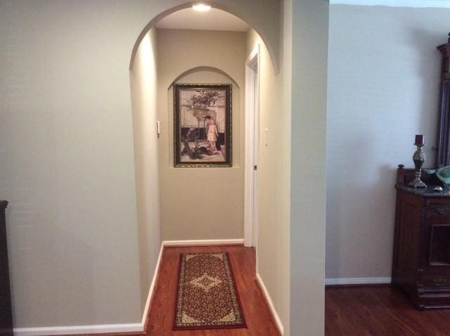 hall featuring baseboards, arched walkways, and wood finished floors