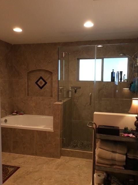 full bath with a relaxing tiled tub, a stall shower, and tile walls