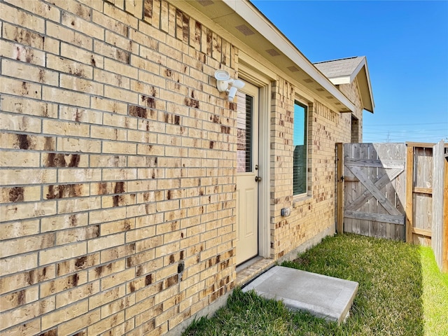 doorway to property with brick siding, roof with shingles, and fence