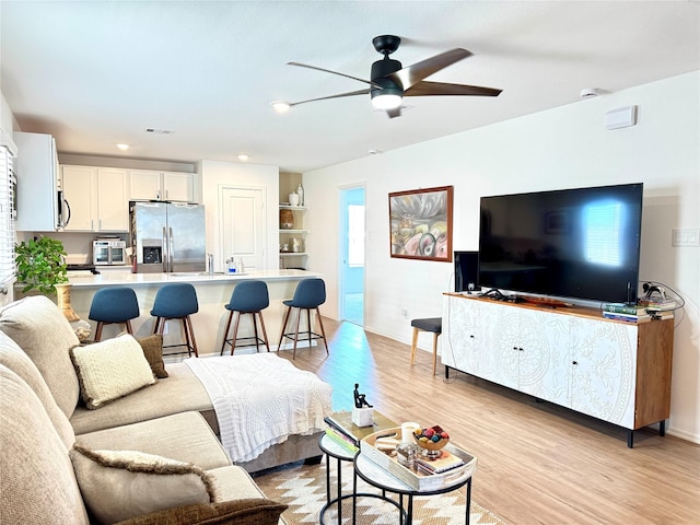 living room with baseboards, visible vents, ceiling fan, and light wood finished floors