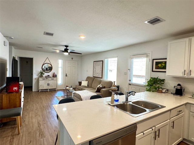 kitchen featuring visible vents, a sink, a peninsula, and dishwasher