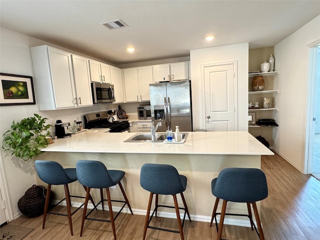 kitchen featuring a breakfast bar area, stainless steel appliances, visible vents, a sink, and a peninsula