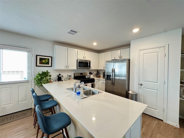 kitchen with appliances with stainless steel finishes, a kitchen breakfast bar, a peninsula, light countertops, and a sink