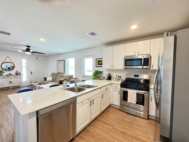 kitchen with visible vents, appliances with stainless steel finishes, open floor plan, a peninsula, and a sink