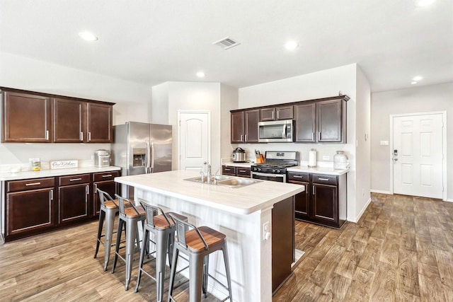 kitchen featuring light wood-style flooring, stainless steel appliances, dark brown cabinetry, a breakfast bar area, and light countertops