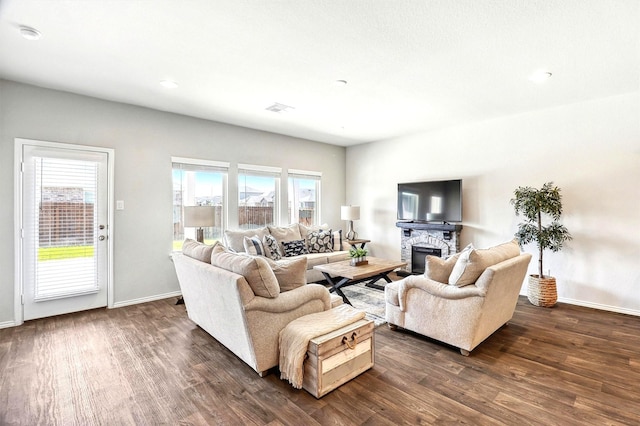 living area featuring visible vents, a stone fireplace, dark wood-type flooring, and baseboards