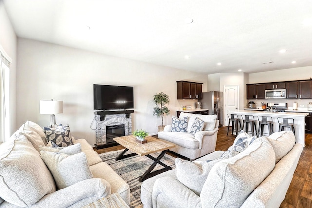 living area featuring a stone fireplace, recessed lighting, and dark wood-style flooring