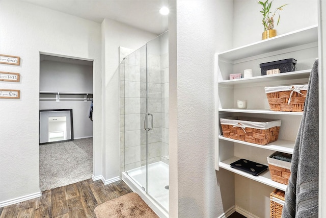 full bathroom featuring a spacious closet, a shower stall, baseboards, and wood finished floors