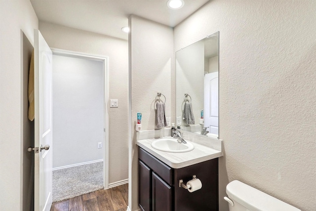 bathroom with toilet, wood finished floors, vanity, and a textured wall