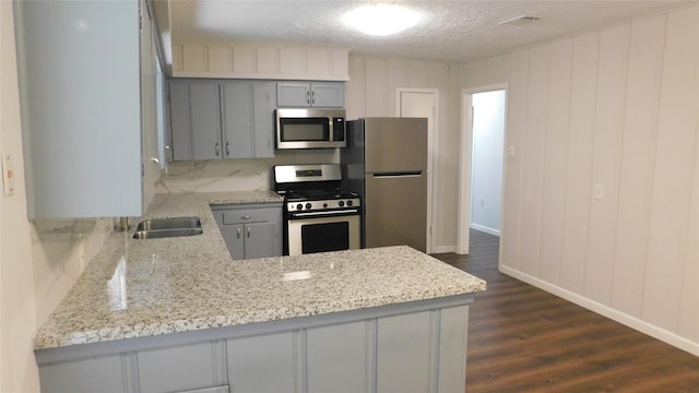 kitchen featuring stainless steel appliances, gray cabinetry, dark wood-type flooring, light stone countertops, and a peninsula