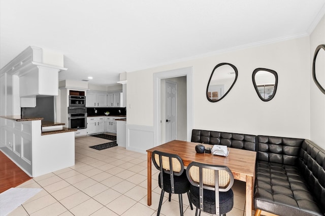 dining space featuring breakfast area, a wainscoted wall, light tile patterned flooring, and crown molding