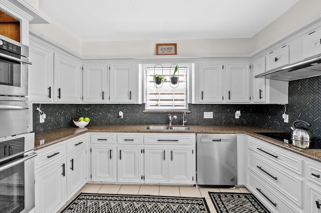 kitchen with light tile patterned floors, a sink, white cabinets, appliances with stainless steel finishes, and dark stone counters