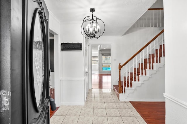 foyer entrance featuring baseboards, ornamental molding, an inviting chandelier, stairs, and light wood-type flooring