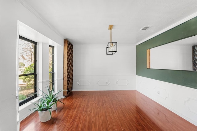 unfurnished dining area with visible vents, crown molding, and wood finished floors