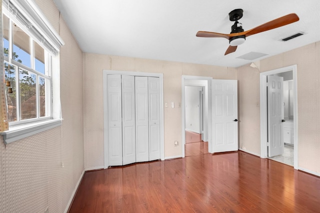 unfurnished bedroom with a closet, wood finished floors, visible vents, and a ceiling fan