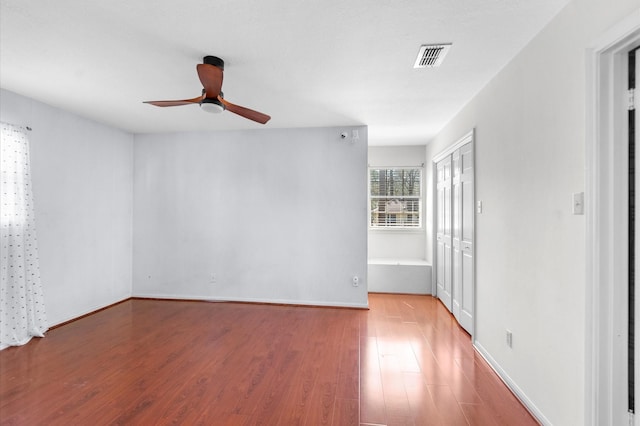 unfurnished room with ceiling fan, wood finished floors, visible vents, and baseboards