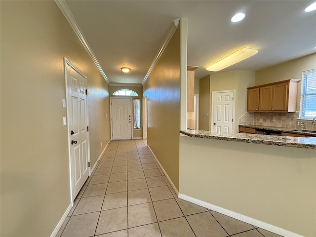 corridor with light tile patterned floors, crown molding, baseboards, and a sink