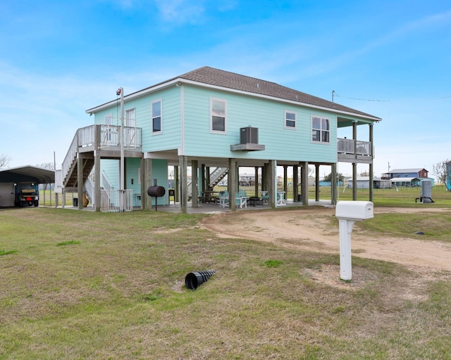 rear view of house with driveway, a lawn, stairway, roof with shingles, and a carport