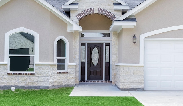 doorway to property featuring a garage, stone siding, a shingled roof, and stucco siding