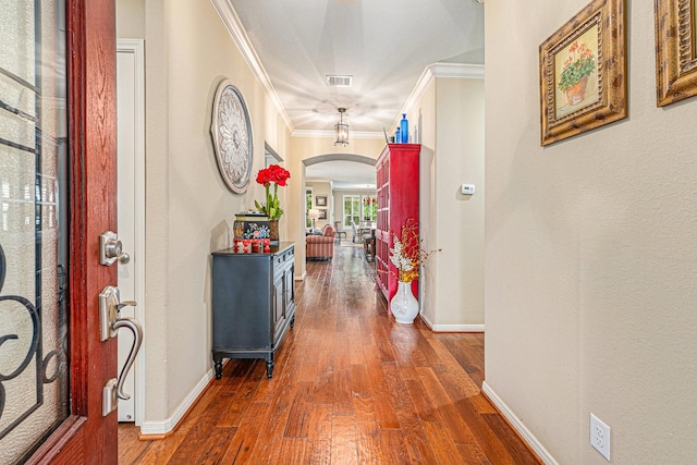 hallway featuring arched walkways, visible vents, baseboards, dark wood finished floors, and crown molding