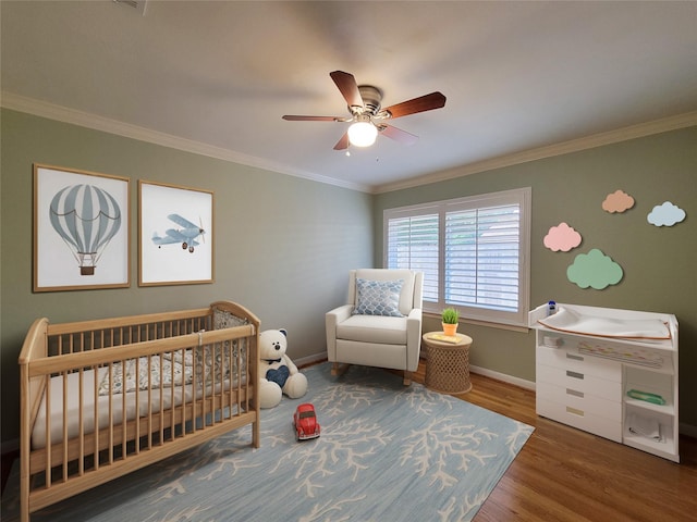 bedroom featuring crown molding, a ceiling fan, wood finished floors, a nursery area, and baseboards