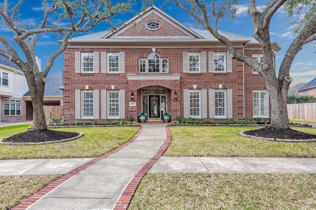 colonial home featuring brick siding, fence, and a front lawn