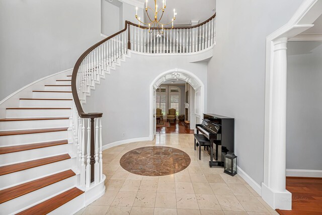 foyer with baseboards, arched walkways, stairs, ornate columns, and a chandelier