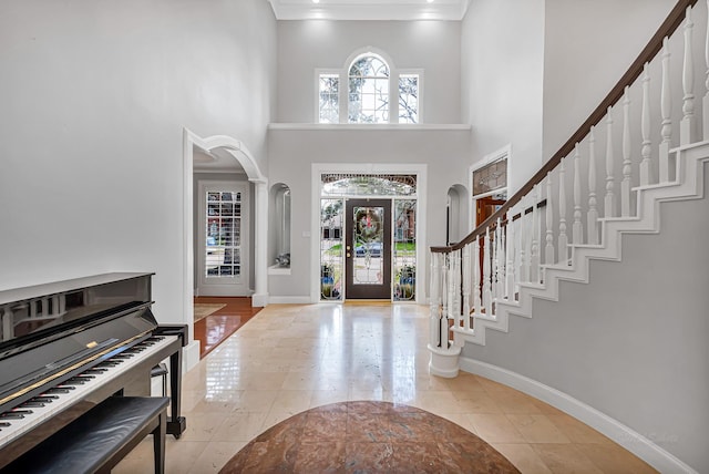 foyer with baseboards, stairway, arched walkways, and a healthy amount of sunlight