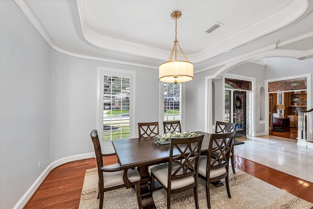 dining area featuring arched walkways, a raised ceiling, wood finished floors, and baseboards