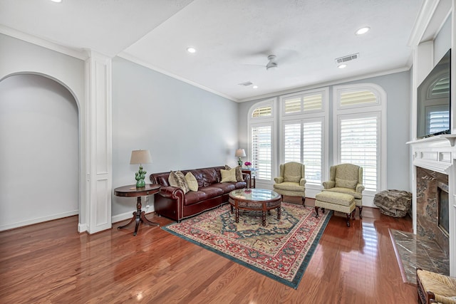 living room featuring a fireplace, wood finished floors, visible vents, baseboards, and ornamental molding