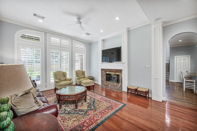 living room with visible vents, arched walkways, ornamental molding, wood finished floors, and a fireplace