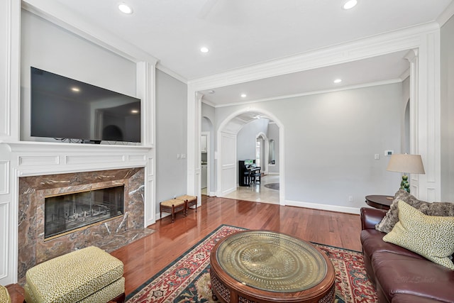 living room with crown molding, arched walkways, wood finished floors, and a high end fireplace