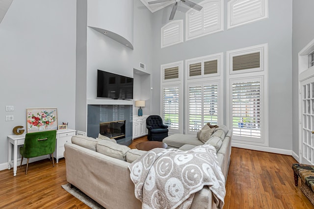 living area featuring wood finished floors, a glass covered fireplace, and baseboards