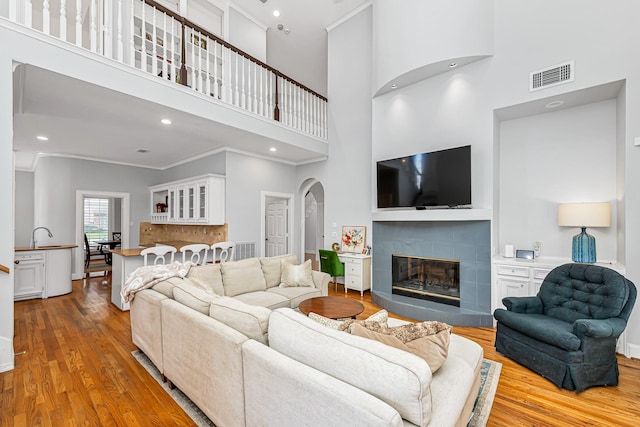 living area with baseboards, visible vents, a tiled fireplace, ornamental molding, and wood finished floors