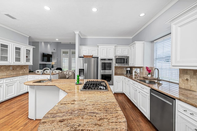 kitchen with appliances with stainless steel finishes, white cabinetry, a sink, and light stone countertops